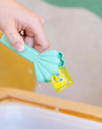 Main tenant une pince vert menthe en forme de coquillage pour saisir un cube jaune Glo Pals au-dessus d’un bac d’eau.